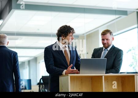 Two business partners in suits discussing new software on laptop together at office Stock Photo