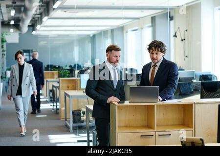 Two office workers in formal wear discussing presentation on laptop standing at office Stock Photo