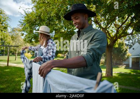 Mixed race male and female farmers hanging out washing on laundry line Stock Photo