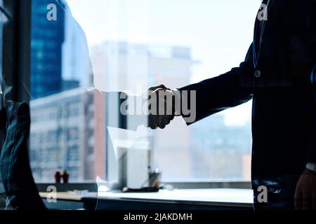 Close-up of two businessmen shaking hands behind glass window while standing at office Stock Photo