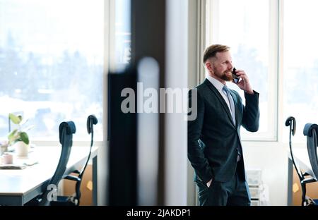 Young bearded manager in formal wear smiling while having conversation on mobile phone at office Stock Photo