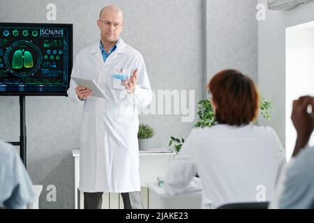 Mature speaker in white coat talking to students and explaining material during lecture Stock Photo