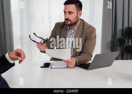 Confident executive discussing over contract with business partner. Male entrepreneurs planning in meeting. They are sitting at office desk. Stock Photo
