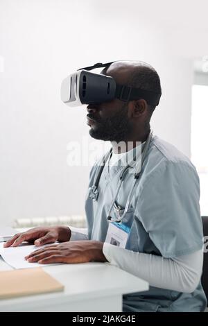 African medical student in uniform using VR glasses while sitting at desk at conference Stock Photo