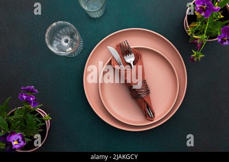 Table setting, empty plate with napkin and cutlery on a green background, top view of the served table decorated with pansies flowers Stock Photo