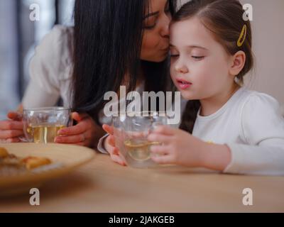 Family drinking tea with cookies on kitchen at home. Mother and daughter having fun, happy moment together at home. Stock Photo