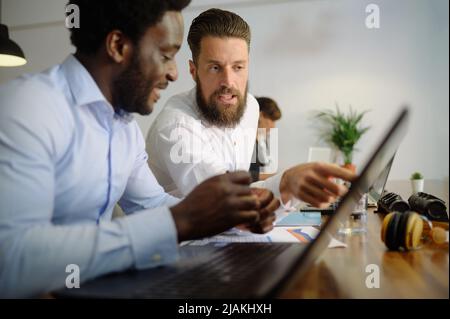 Diverse businessmen working on laptop together in office Stock Photo