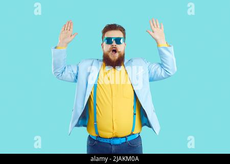 Funny fat man in party suit and sunglasses pretends to be scared and raises his hands up Stock Photo