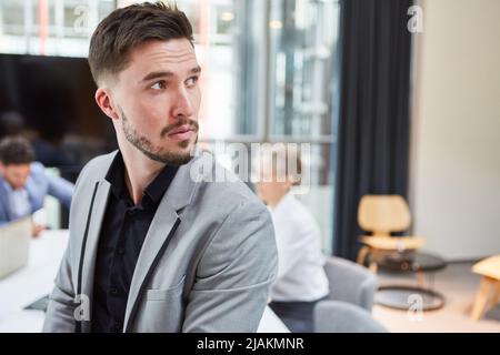 Young businessman looking over shoulder with skepticism and questioning in meeting in office Stock Photo