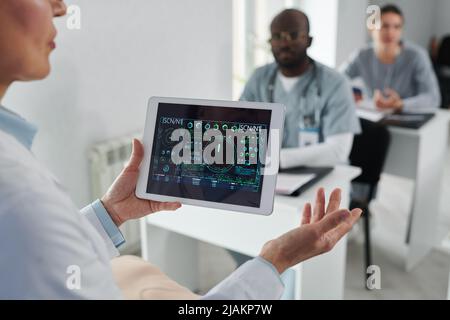 Close-up of mature lecturer holding digital tablet with graphs in his hands and talking to students during medical training Stock Photo