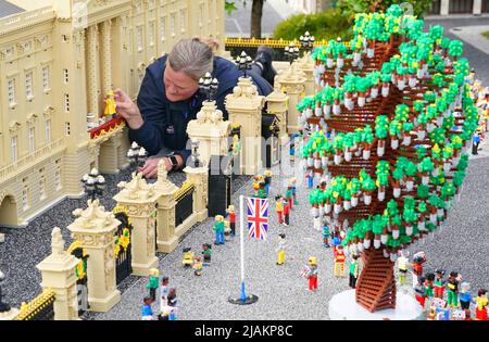 Model Maker Paula Young places a LEGO replica of Queen Elizabeth II, along with other members of the Royal Family, in a display replicating the Royal Balcony scene at Buckingham Palace for the LEGOLAND Resort's Platinum Jubilee Display that was unveiled today. All members of the Royal family took 8 hours to build and are made up of over 200 LEGO Bricks. LEGOLAND Windsor Resort today unveiled its royal-inspired models to celebrate the Queen's Platinum Jubilee. The overall number of bricks used was 18,001 and the models took a total of 281.5 hours to finish. The display also includes includes a  Stock Photo