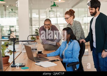 Diverse group of smiling businesspeople working together around a laptop Stock Photo