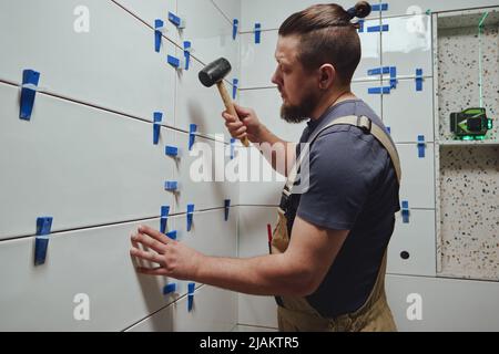 Tiler knocks the wedges of the ceramic tile leveling system off the wall in the bathroom Stock Photo