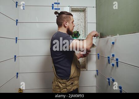 Repairman applying tile adhesive with a trowel on the bathroom wall Stock Photo
