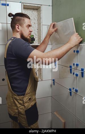 Tiler laying installing ceramic tiles on the wall in the bathroom Stock Photo