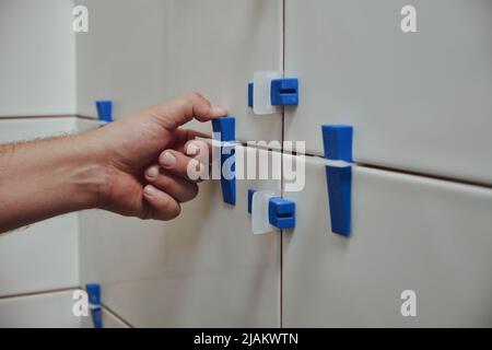 Tiler using tile leveling system when laying ceramic tiles on bathroom wall Stock Photo