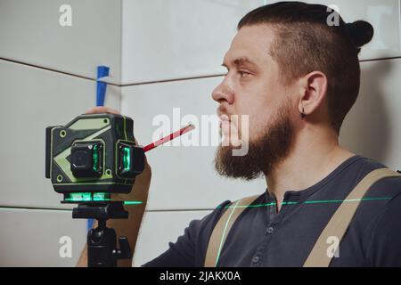 Tiler checks tile laying with building measuring laser level Stock Photo
