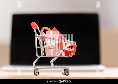 Toy shopping cart with gift boxes near blurred laptop Stock Photo