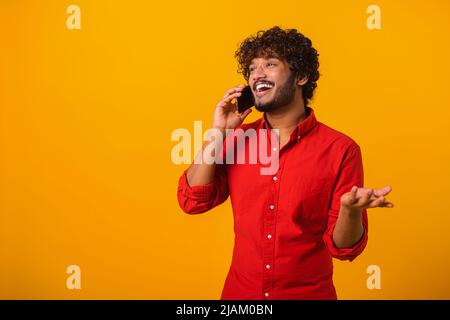 Mobile communication. Portrait of man making call to consult, having pleasure talk on cellphone, discussing great news. Indoor studio shot isolated on orange background Stock Photo