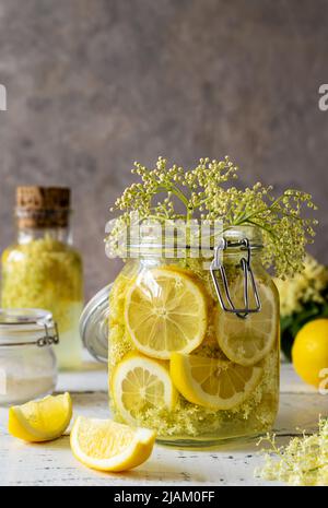 Elderberry infused water or syrup made with fresh flowers and lemons as basic ingredients. Grey background Stock Photo