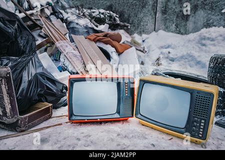 Old TVs thrown into the trash. Two bright color televisions in the middle of a pile of rubbish. Stop watching TV and obsolescence of technology theme Stock Photo