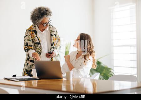 Mature manager having a discussion with her colleague in a meeting room. Two creative businesswomen collaborating on a new task in a woman-owned start Stock Photo