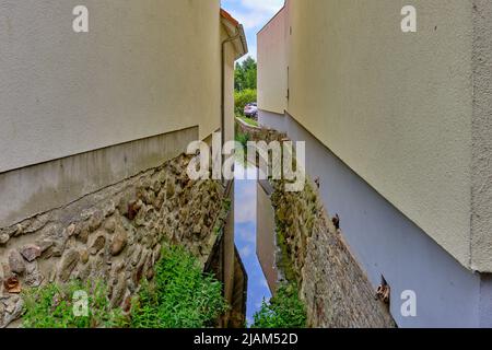 Narrow gap between two houses through which a small stream flows; in the historic town centre of Waren, Mecklenburg-Western Pomerania, Germany. Stock Photo