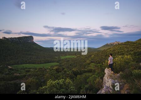 A man standing on the cliff edge, looking over the Pic Saint-Loup and Pic de l'Hortus, two famous mountains in the south Fance Stock Photo