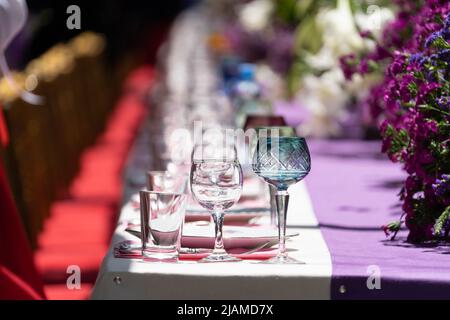 Laid big table with empty dishes near red chairs for holiday on outdoor in sun weather. Soft focus. Stock Photo