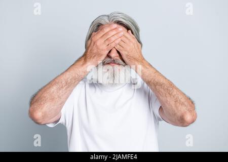 Photo of tired stressed man pensioner dressed white t-shirt arms cover eyes avoiding bright light isolated grey color background. Stock Photo