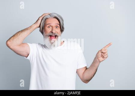 Photo of impressed funky man pensioner dressed white t-shirt arm head pointing finger empty space isolated grey color background. Stock Photo