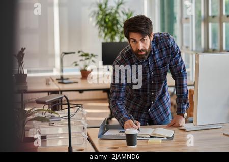 Focused businessman leaning over his desk and writing in a notebook Stock Photo