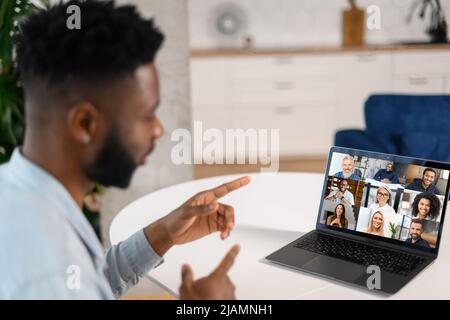 Morning meeting on the distance. African-American man using laptop for virtual communication with diverse work team, multiracial employees using new platform for chatting and brainstorming online Stock Photo