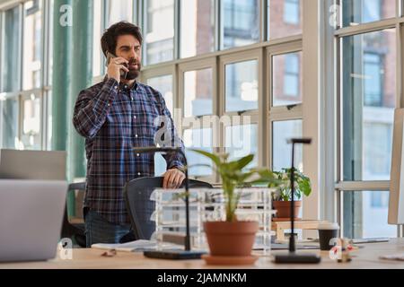 Businessman standing at his office desk and talking on a phone Stock Photo