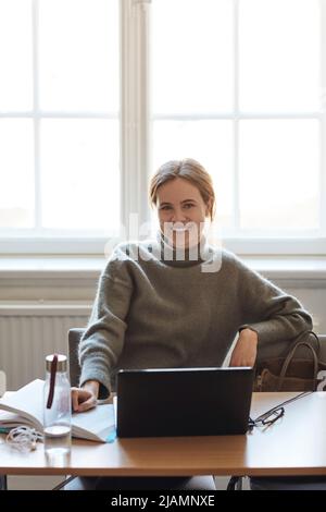Portrait of confident female student with laptop sitting at desk in classroom Stock Photo