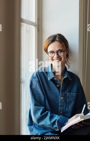 Portrait of happy female student with book by window Stock Photo