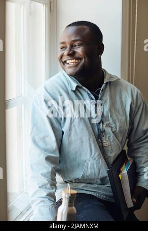 Happy male student with book and laptop looking through window at university Stock Photo