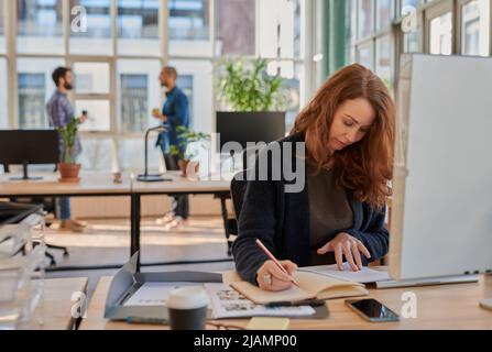 Businesswoman working at her office desk with colleagues in the background Stock Photo
