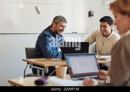 Smiling teacher and student looking at laptop while sitting in classroom Stock Photo