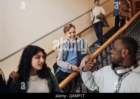 Smiling male student talking with friend while leaning on railing in university Stock Photo