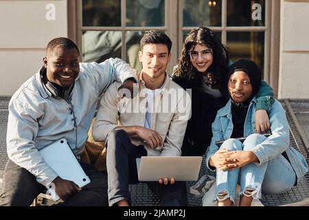 Portrait of multiracial students with laptop sitting at university campus Stock Photo