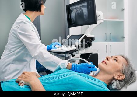 Ultrasound diagnostics of thyroid gland. Endocrinologist making ultrasonography to senior female patient at ultrasound office of medical clinic Stock Photo