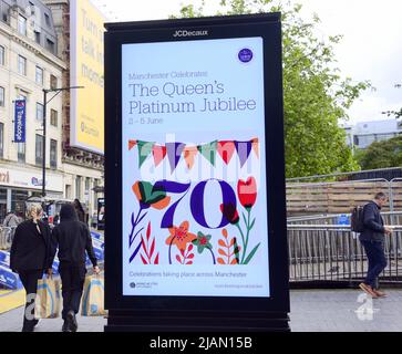 Manchester, UK, 31st May, 2022. People walk past an electronic sign advertising Jubilee events in Manchester, UK. Queen's Platinum Jubilee preparations, in Manchester, England, United Kingdom. In 2022, Her Majesty The Queen will become the first British monarch to celebrate a Platinum Jubilee after 70 years of service. The Platinum Jubilee Central Weekend takes place from 2nd to 5th June. Friday 3rd June is an extra Bank Holiday, resulting in a four-day bank holiday weekend. Credit: Terry Waller/Alamy Live News Stock Photo