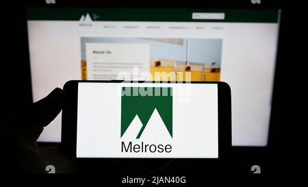 Person holding smartphone with logo of British company Melrose Industries plc on screen in front of website. Focus on phone display. Stock Photo