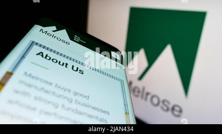 Smartphone with webpage of British company Melrose Industries plc on screen in front of business logo. Focus on top-left of phone display. Stock Photo