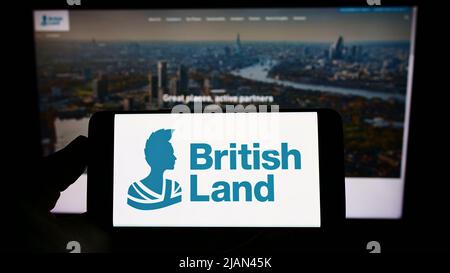 Person holding cellphone with logo of company The British Land Company plc on screen in front of business webpage. Focus on phone display. Stock Photo