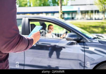 Taxi phone app for cab or car ride share service. Customer waiting driver to pick up on city street. Man holding smartphone. Mobile and online booking. Stock Photo