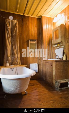 White freestanding roll top bathtub and antique furnishings in bathroom inside old circa 1840 Canadiana cottage style fieldstone home. Stock Photo