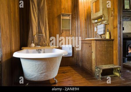 White freestanding roll top bathtub and antique furnishings in bathroom inside old circa 1840 Canadiana cottage style fieldstone home. Stock Photo