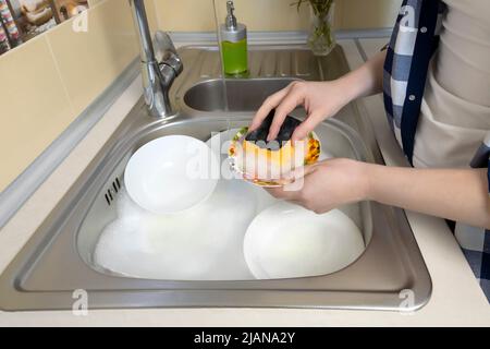 Girl washes a lot of dirty dishes in the kitchen sink. Stock Photo